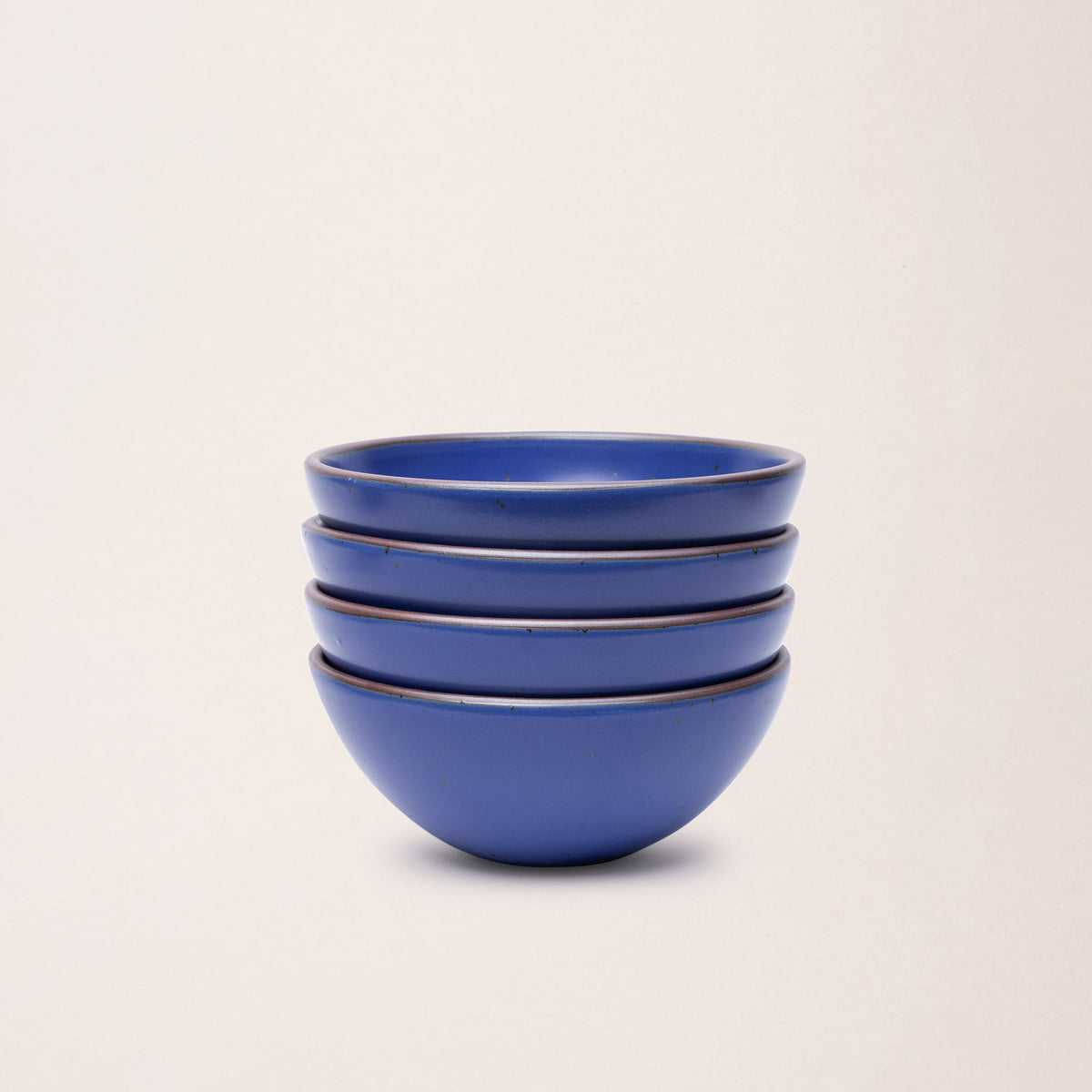 A stack of 4 medium rounded ceramic bowls in a cobalt blue color featuring iron speckles and an unglazed rim