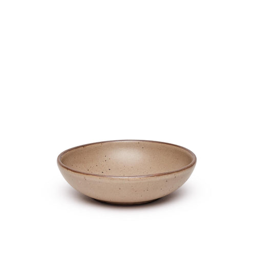 A dinner-sized shallow ceramic bowl in a warm pale brown color featuring iron speckles and an unglazed rim