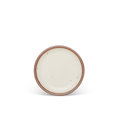 A dessert sized ceramic plate in a warm off-white color featuring iron speckles and an unglazed rim