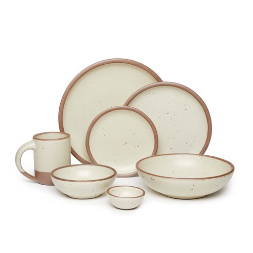 The Mug, bitty bowl, breakfast bowl, everyday bowl, cake plate, side plate and dinner plate paired together in a warm, tan-toned, off-white color featuring iron speckles